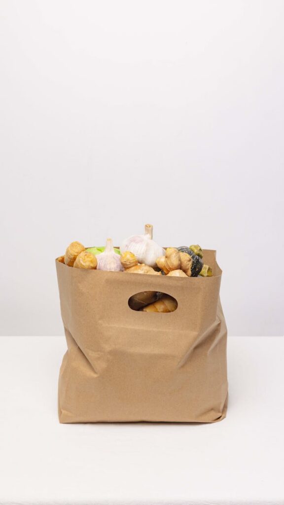 A paper bag filled with various fresh vegetables including garlic and squash, promoting sustainable packaging.